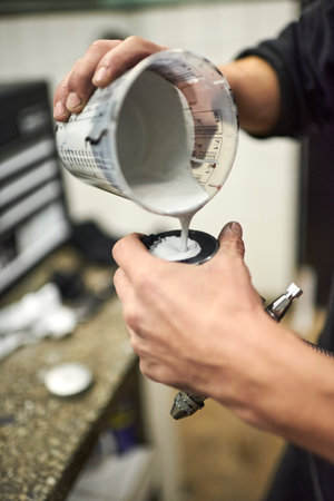 Hands of a young unrecognizable man pouring paint into a spray paint gun tank in his workshop. Close up view.の写真素材