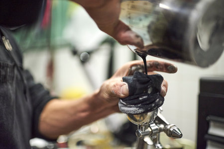 Hands of a young unknown person pouring paint into a spray paint gun tank in his workshop. Low angle...