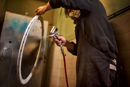 Unrecognizable person using a protective mask spray painting a bicycle rim in his bike workshop. Low angle view.の写真素材
