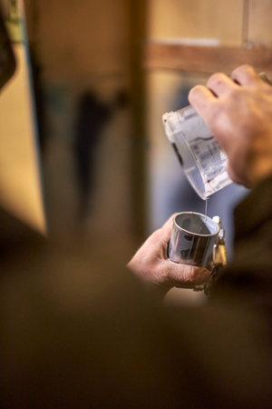 Hands of a young unrecognizable man pouring paint into a spray paint gun tank in his workshop. Close up composition with copy space.の写真素材