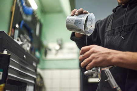 Young unrecognizable person pouring paint into a spray paint gun tank in his workshop. Close up view...