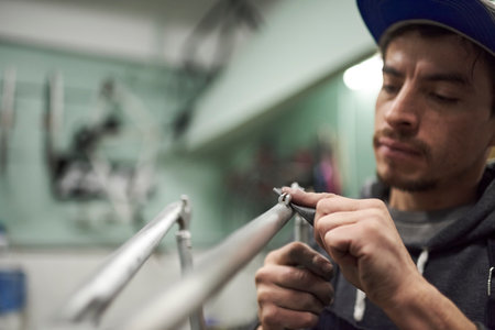 Latin worker sanding an unpainted bicycle frame as part of the process of a bike renovation work done at his workshop. Composition with selective focus on the hands and copy space.の写真素材