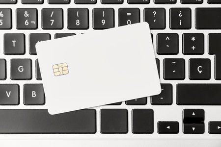 Blank white credit or debit card with microchip on a laptop keyboard. Concepts of plastic money and online shopping. Top view composition without people.の写真素材