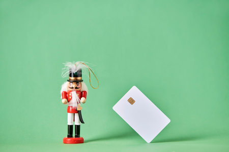 Traditional colorful wooden Christmas nutcracker in red suit with a green background and a blank credit or debit bank card. Concept: Holidays shopping using plastic money.の写真素材