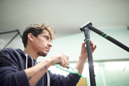 Latin young man preparing a bicycle frame with masking tape for a custom painting design in his bike...