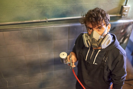 Latin man wearing a protective mask spray painting a bicycle in his workshop. High angle view,...