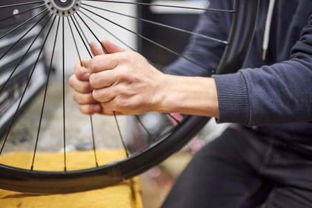 Unrecognizable man checking the tension of the spokes of a bicycle wheel in his bike workshop. Real people at work.の写真素材