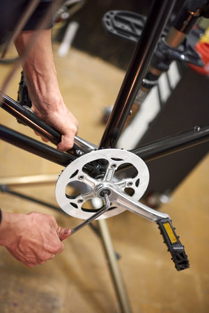 Maintenance service of a bicycle: hands of an unknown repairman assembling the pedals of a bike at...