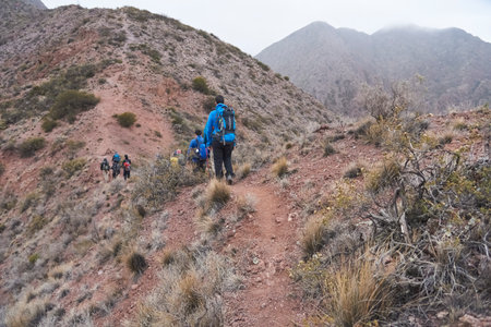 Group of unrecognizable hikers seen from behind walking through a mountainous arid landscape in...