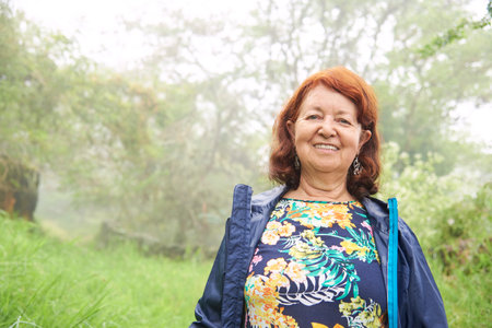 Active mature Hispanic woman smiles happily looking at camera, enjoying a morning walk in nature,...