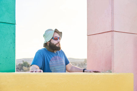 Portrait of a young bearded man, wearing a sun hat and sunglasses, with his eyes closed.