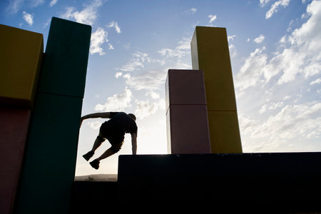 Backlight silhouette of an active man jumping between concrete blocks practicing parkour, an athletic urban sport popular among young people.の写真素材