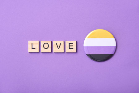 Wooden pieces with letters form the word Love beside a flag badge symbol of the non binary community. Purple background. Conceptual image supporting equality and against discrimination.の写真素材