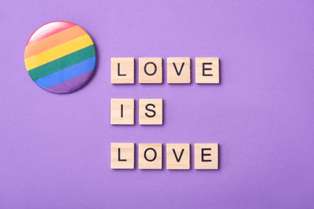 Wooden pieces with letters form the text Love is Love next to a rainbow flag badge, symbol of LGBT...