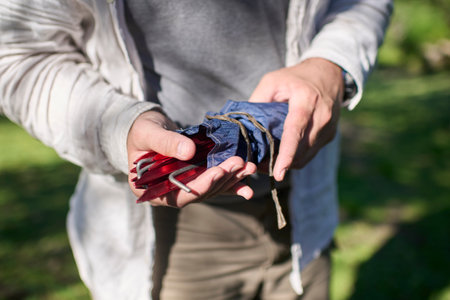 Unrecognizable person taking tent pegs out of a small bag for the tent he is setting up outdoors, in a natural, quiet, green and sunny environment.の写真素材