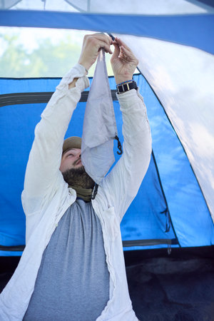 Young male traveler setting up a blue tent for camping in a natural area during his trip.の写真素材
