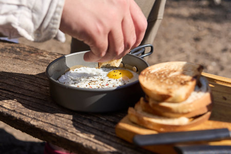 Unknown traveler eating breakfast outdoors, fried eggs and toasted bread slices. Close up...