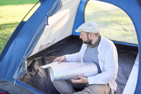 Young traveler opening his insulating mat to rest comfortably inside his tent while camping in a wilderness campsite.の写真素材