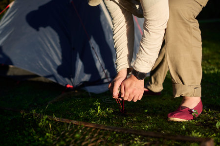 Unrecognizable person setting up camp at dusk. His shadow is cast on the tent, already set up behind him.の写真素材