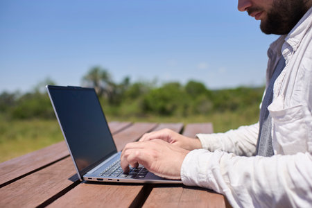 Unrecognizable man working on his laptop at an outdoor table on a sunny day. Concept: digital nomad working remotely while traveling enjoying a lifestyle of freedom.の写真素材