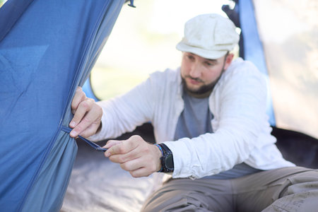 Young male traveler tying open the door of his blue tent, pitched in a camping site in the nature.の写真素材