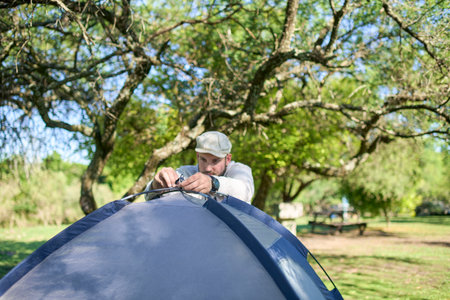 Man tying the poles of his tent, in the process of setting it up outdoors, in a natural, quiet, green and sunny environment.の写真素材