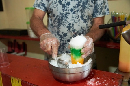 Unrecognizable man preparing a raspado, a refreshing and colorful Colombian snack composed of crushed ice with different sweet flavors and sauces or toppings.の写真素材