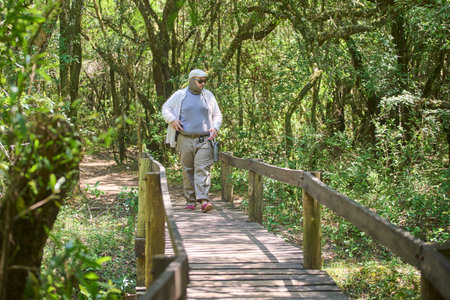 Hispanic man crossing a wooden bridge in El Palmar National Park, in Entre Rios, Argentina. Concepts: ecotourism, enjoyment of outdoor leisure time, wellbeing of being in contact with natureの写真素材