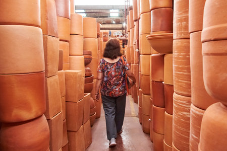 Unrecognizable woman walking in an aisle formed by stacks of ceramic pots in a store in Raquira, Boyaca, Colombia, a tourist town known for its craftsmanship and its pottery.の写真素材