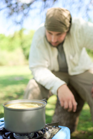 Male traveler waiting for his meal to be ready, rice with vegetables that he is cooking using a portable gas stove, at his campsite. Composition with selective focus on the pot.の写真素材