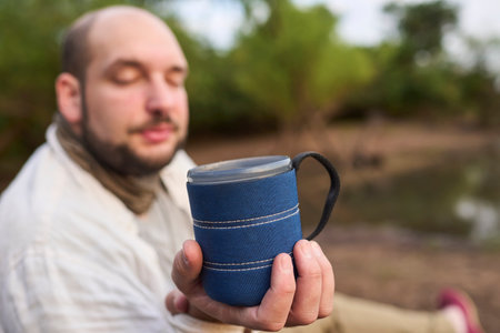 Man offers towards the camera a cup of freshly brewed coffee in nature, early in the morning. His expression is one of tranquility, calm and well-being. El Palmar National Park, Entre Rios, Argentina.の写真素材