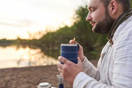 Hispanic man having breakfast, enjoying a cup of freshly brewed coffee with cookies on the bank of a stream at sunrise. El Palmar National Park, Entre Rios, Argentina.の写真素材