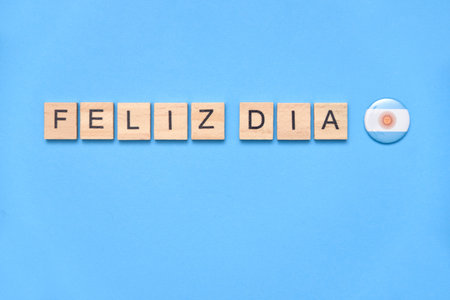 Text in Spanish Happy day with an Argentine national flag pin, on a light blue background.