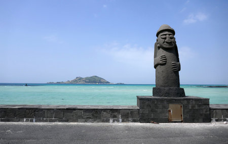 Jeju Island, South Korea - April 17, 2018 : Dol hareubang stone statue in front of a turquoise sea with volcanic island.のeditorial素材