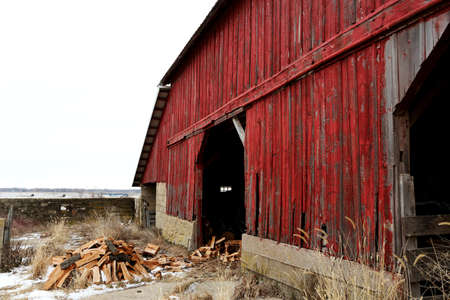 An old red barn with firewood in front
