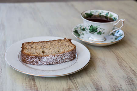 Cup of tea in antique bone china teacup with banana bread on white plate