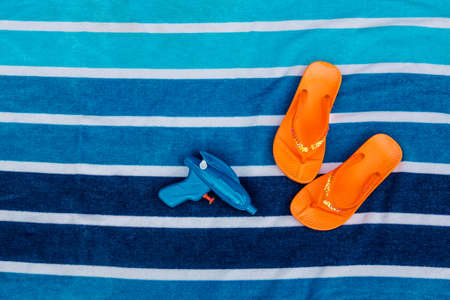 Orange flip flops and squirt gun on beach towel next to poolの写真素材