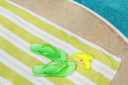 Green flip flops and squirt gun next to a poolの写真素材