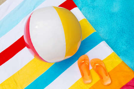 Flip flops and a beach ball on a striped towel next to a poolの写真素材