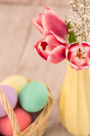 Pink tulips in a vase with a basket of colorful Easter eggs