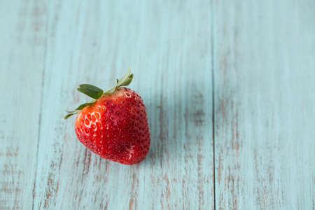 Single strawberry on blue wood painted backgroundの写真素材