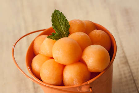 Cantaloupe balls in orange bucket with mint leaf close upの写真素材