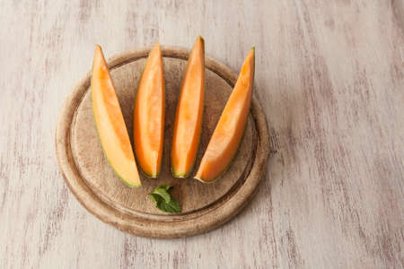 slices of cantaloupe on wood cutting board with mint leafの写真素材