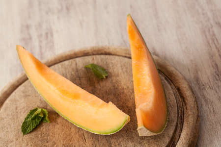Cantaloupe slices on wood cutting board with mint leavesの写真素材