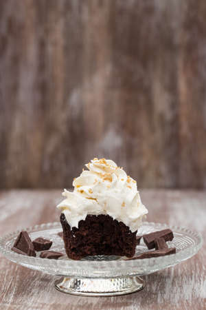 Chocolate cupcake with vanilla frosting missing a bite on antique glass plate with chocolate piecesの写真素材