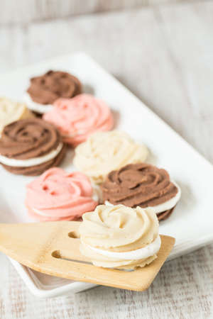 Vanilla strawberry and chocolate cookies on white ceramic platter with wood spatula