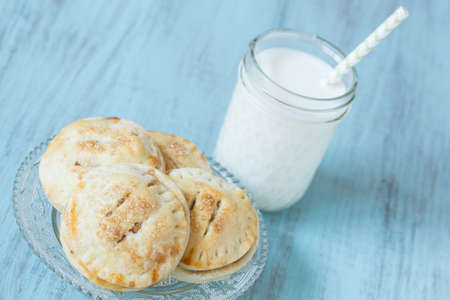 Close up of small autumn apple hand pies with glass of milk with straw