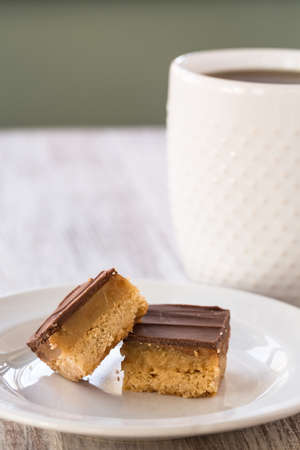 Millionaire bars caramel and chocolate shortbread cookie candy bar with cup of coffee verticalの写真素材