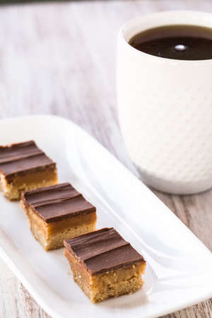 Chocolate and caramel Millionaire Bar candy cookies on white tray with coffeeの写真素材