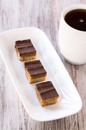 Millionaire bars caramel and chocolate shortbread cookie candy bars on white trayの写真素材